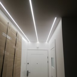 Tantum Optima - Nowoczesne oświetlenie sufitowe LED w przedpokoju we Wrocławiu, z widoczną białą ścianą zabezpieczoną kartonem podczas remontu i białymi drzwiami.