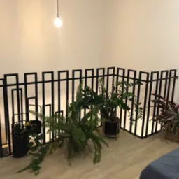 Czarna, metalowa barierka o nowoczesnym designie z kwadratowymi elementami, otoczona roślinami doniczkowymi w jasnym wnętrzu.