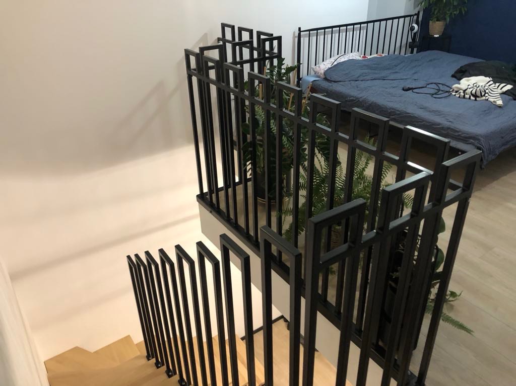 Nowoczesna, czarna, metalowa konstrukcja zabezpieczająca schody i antresolę, z roślinami doniczkowymi w tle.