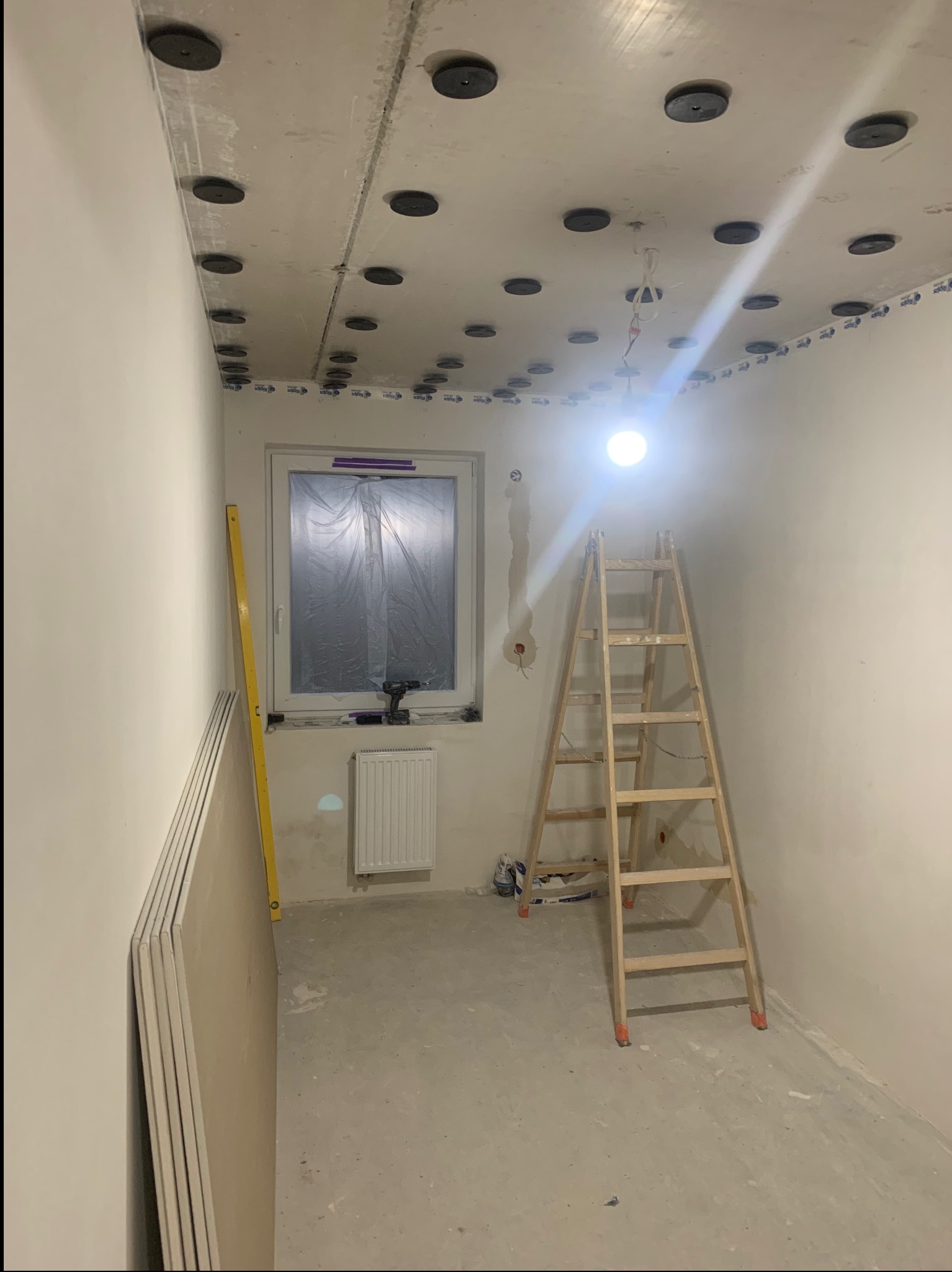 Sufit podwieszany na etapie montażu w pomieszczeniu w Poznaniu. Widoczne płyty karton-gips, drabina i narzędzia. Okno zabezpieczone folią.