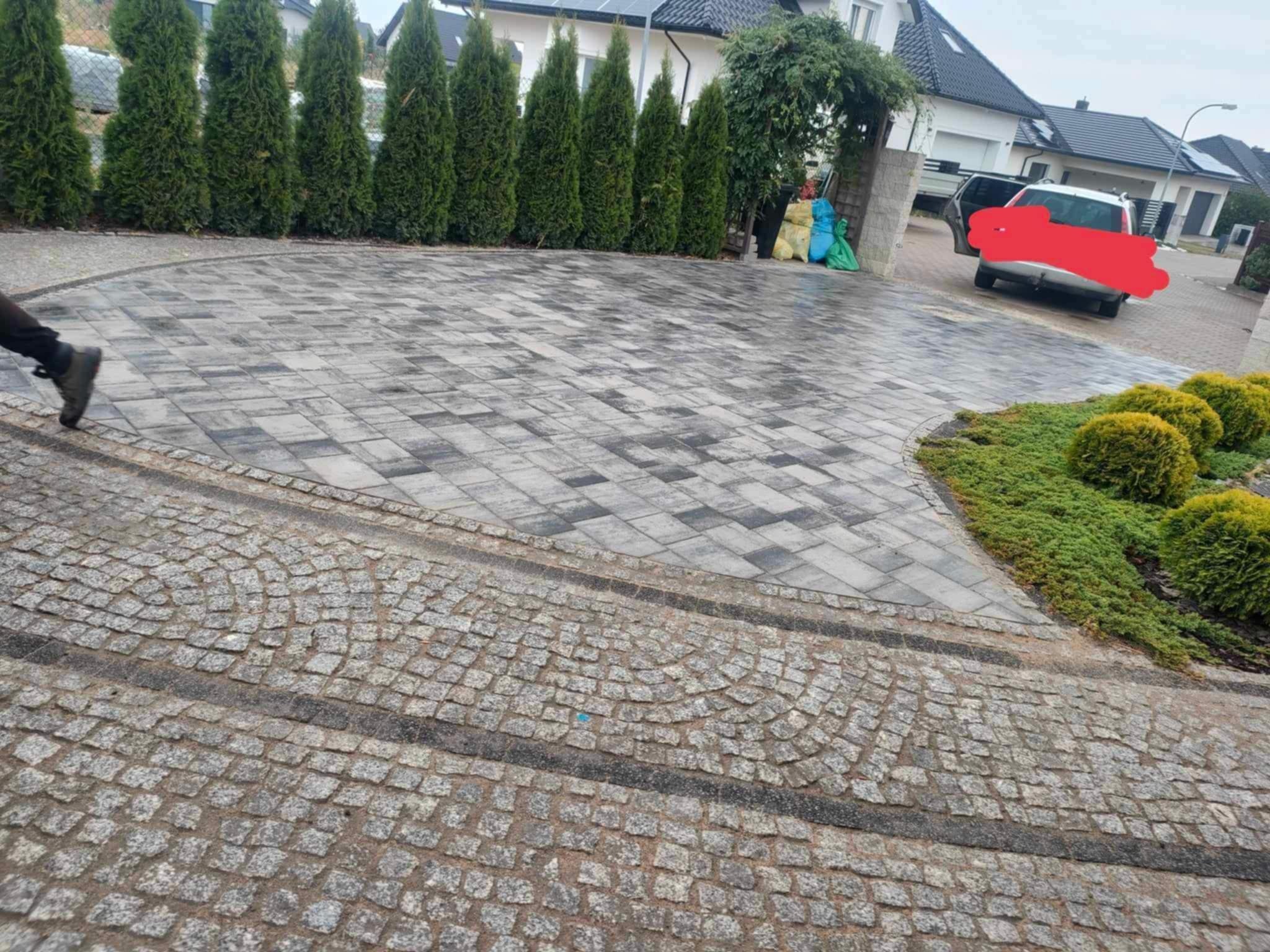 Ułożona z kostki granitowej i brukowej podjazd z zielenią. Elementem wyróżniającym jest osoba wchodząca w kadr.