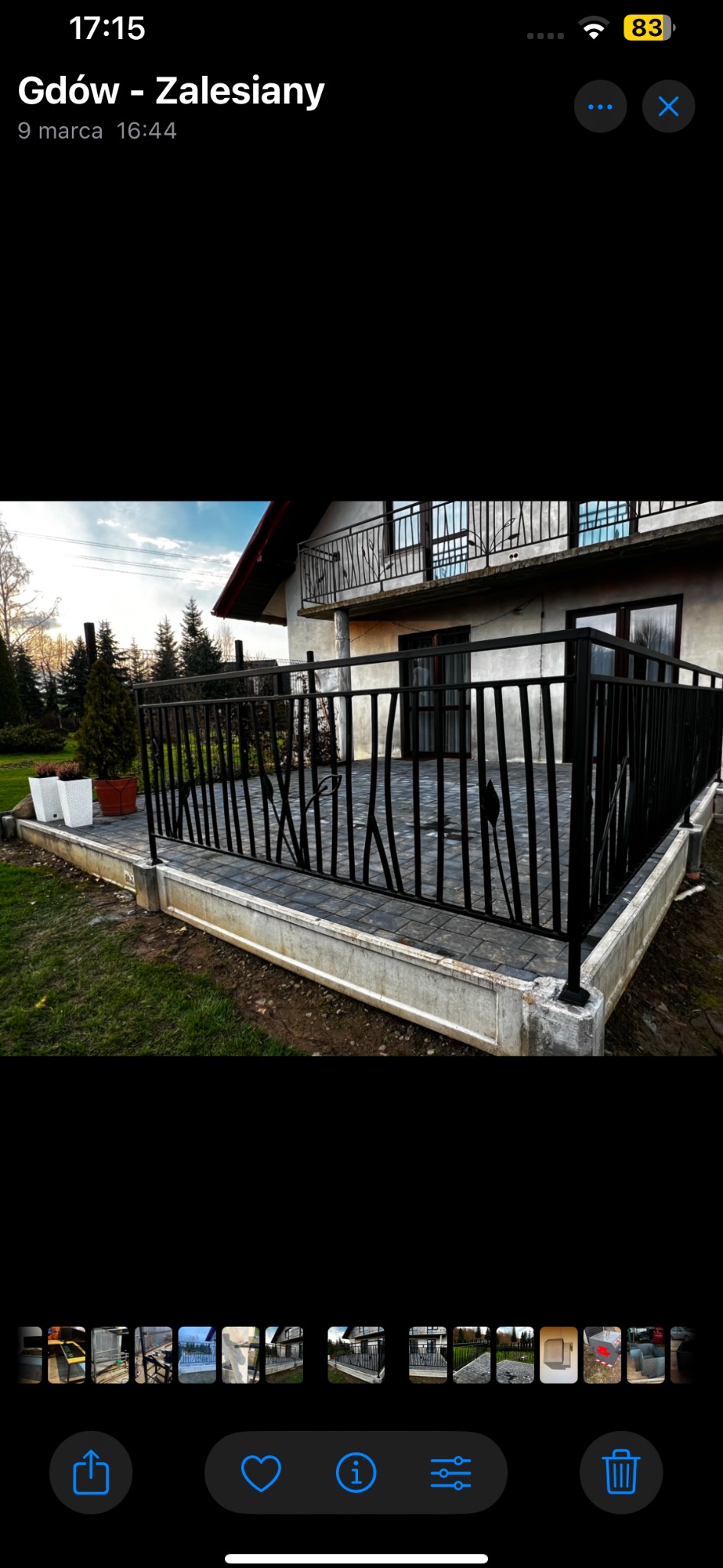 Czarna, metalowa balustrada z motywem liści na tarasie domu jednorodzinnego, widok z zewnątrz na tle zieleni i elewacji.