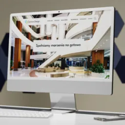 Ekran komputera iMac prezentuje stronę internetową Carriere Design z widokiem na eleganckie wnętrze hotelu lub biurowca; roślina doniczkowa, klawiatura i długopis na białym biurku...