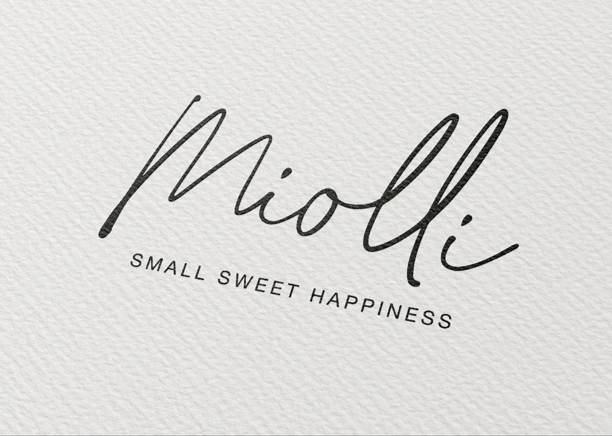 Eleganckie logo 'Miolli' wykonane odręcznym pismem w kolorze czarnym, z dopiskiem 'SMALL SWEET HAPPINESS' małymi literami poniżej, na teksturowanym, białym tle imitującym papier.