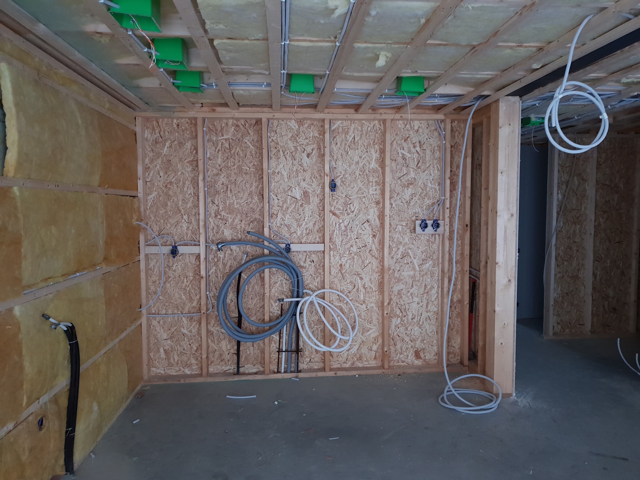 Wnętrze domu szkieletowego w trakcie budowy, widoczne ocieplone ściany, drewniana konstrukcja, puszki elektryczne w suficie oraz rozprowadzone przewody instalacji elektrycznej.