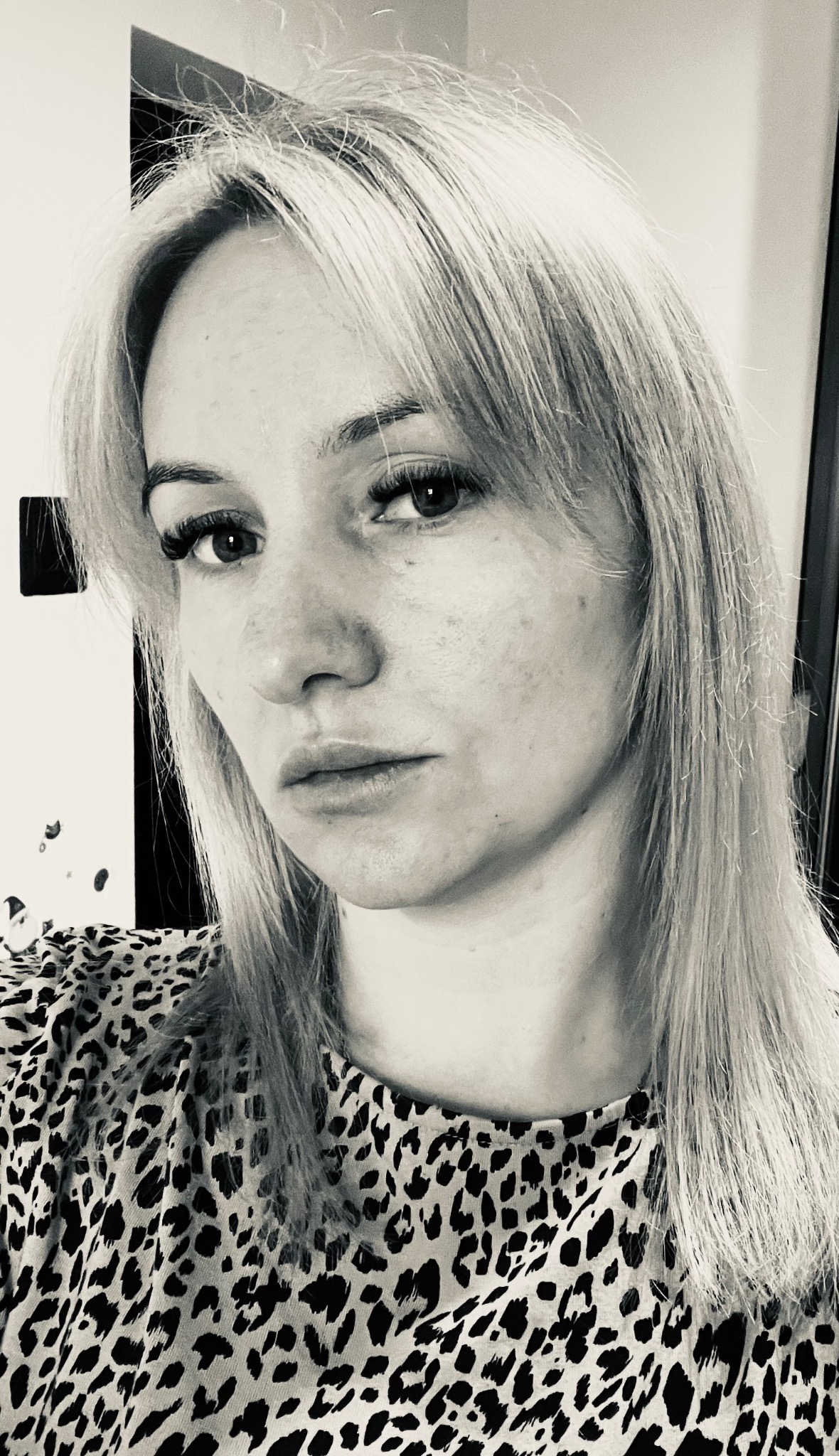 Portret kobiety z blond włosami w bluzce w panterkę, czarno-białe zdjęcie z wyraźnymi piegami.