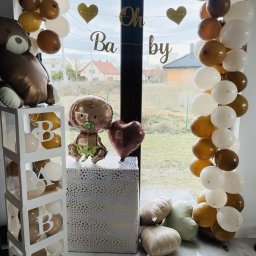 EventMagic - Dekoracja balonowa na przyjęcie baby shower w odcieniach brązu, bieli i złota, z balonami w kształcie misia, bobasa i serca, oraz napisem 'Oh Baby' na tle okna.