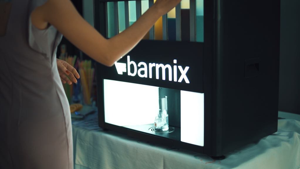 Obsługa automatycznego dystrybutora drinków 'barmix' podczas imprezy, widoczny szklanka z lodem w podświetlanej wnęce.