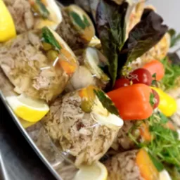 Galaretki z mięsem i warzywami, udekorowane cytryną, papryką i zielonymi listkami na srebrnej tacy, prezentowane pod kątem.