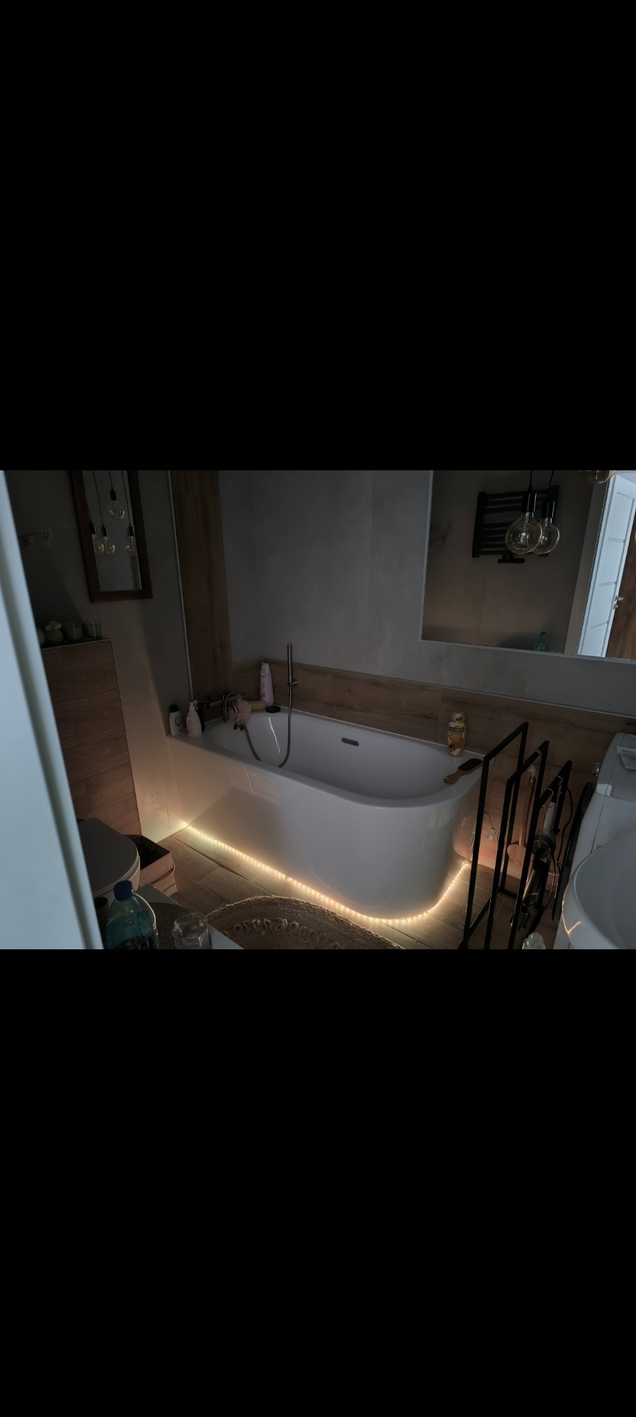 Nowoczesna łazienka z podświetloną wanną, drewnopodobne płytki i minimalistyczne dodatki. Ciepłe światło tworzy przytulną atmosferę.