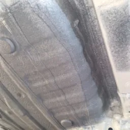 Szare, zabezpieczone podwozie auta z widocznymi elementami konstrukcyjnymi i śladami po nałożonym środku ochronnym, z bliska.