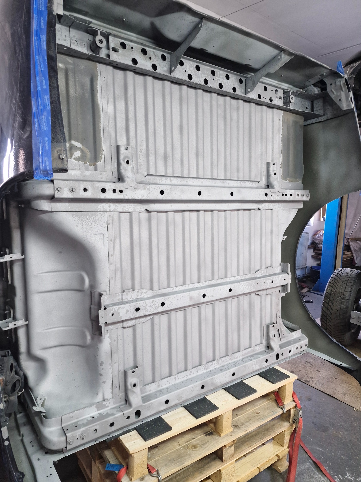 Podwozie samochodu po oczyszczeniu i wstępnym malowaniu antykorozyjnym, umieszczone na drewnianej palecie w warsztacie.