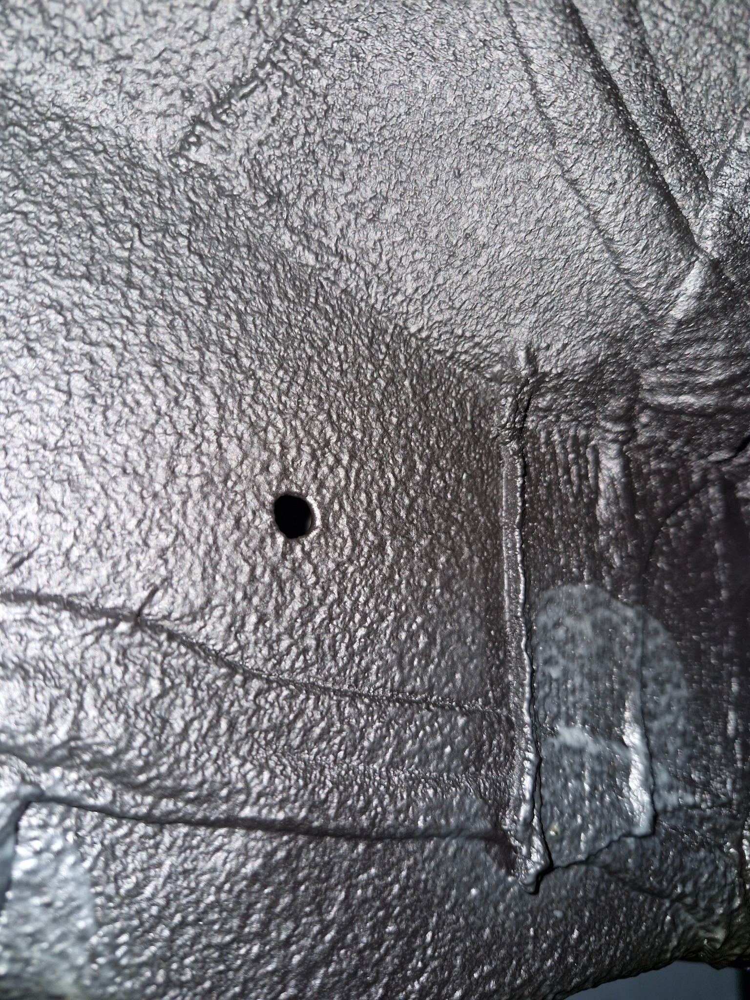 Szczegółowe ujęcie podwozia pojazdu po nałożeniu zabezpieczenia antykorozyjnego, widoczna faktura i otwór technologiczny.