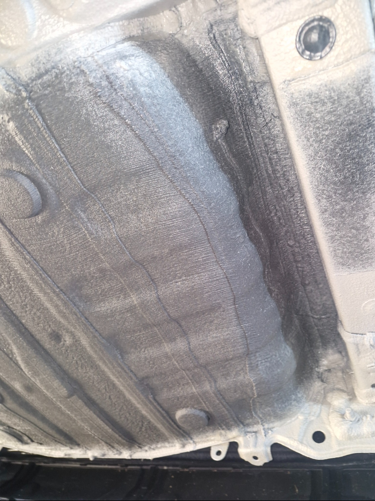 Szare, zabezpieczone podwozie auta z widocznymi elementami konstrukcyjnymi i śladami po nałożonym środku ochronnym, z bliska.