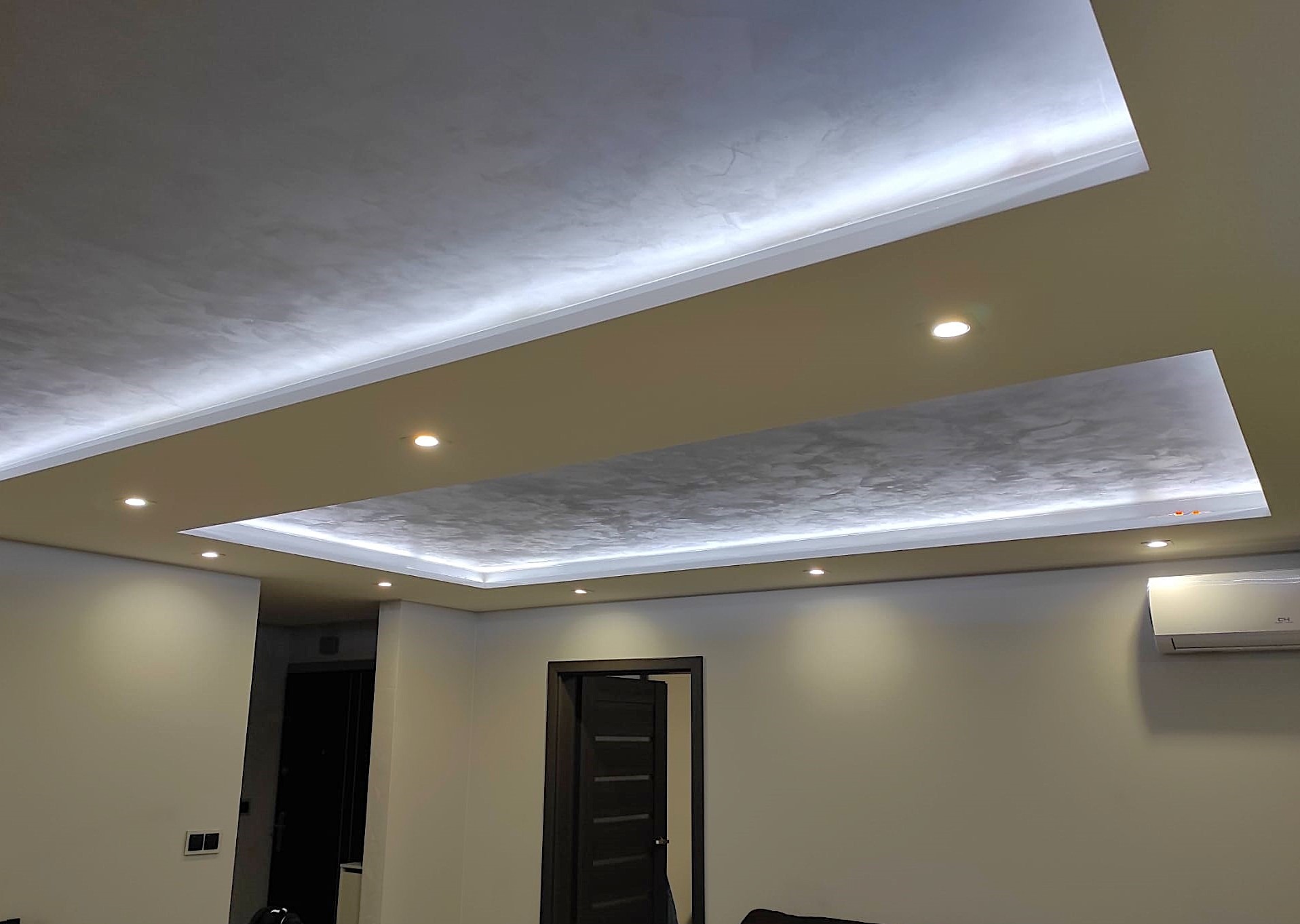 Sufit podwieszany z oświetleniem LED i dekoracyjną fakturą, widoczne punkty świetlne i klimatyzator na ścianie.