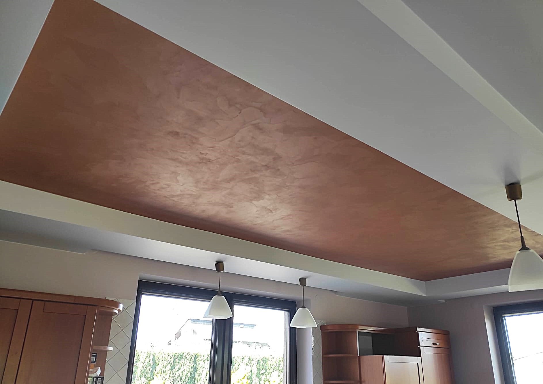 Fragment sufitu z dekoracyjną, brązową fakturą przypominającą trawertyn, oświetlony wiszącymi lampami, widok z dołu, fragment zabudowy kuchennej w tle.