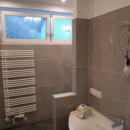 WEBEKO Maciej Paśnik - Nowoczesna łazienka z szarymi płytkami, białym grzejnikiem drabinkowym, umywalką i oknem z widokiem na zewnątrz. Na umywalce pudełko z urządzeniem pomiarowym.