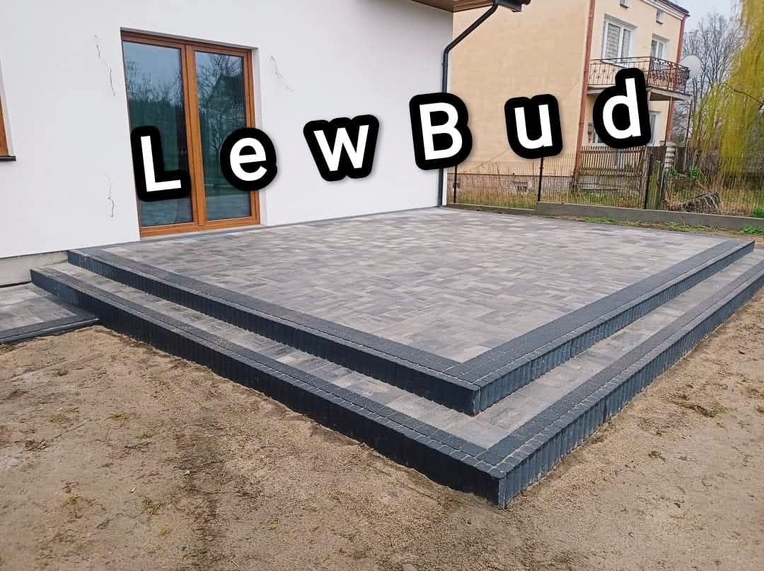 Wykończony taras z kostki brukowej z dwoma stopniami, obrzeża w ciemniejszym odcieniu, widok na dom z oknem i fragmentem elewacji, na zdjęciu widoczne logo firmy LewBud.