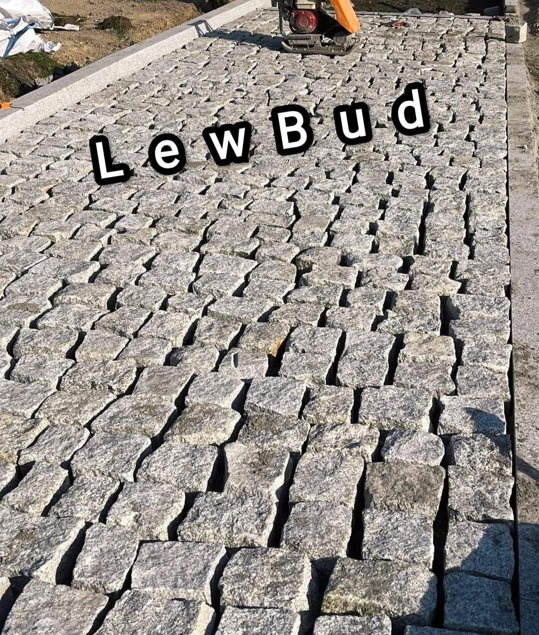 Szara kostka brukowa ułożona w równy wzór, widoczna zagęszczarka i logo firmy 'LewBud' nałożone na zdjęcie.