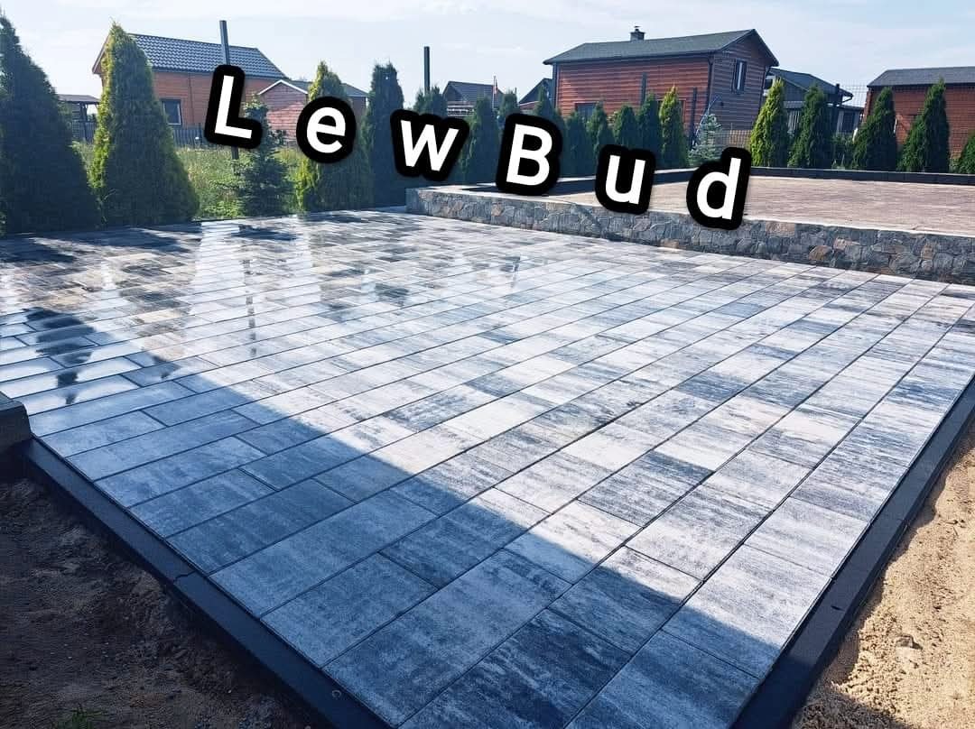 Ułożona kostka brukowa w odcieniach szarości i bieli tworząca wzór na podwórku, widoczne drzewa iglaste i budynek w tle.