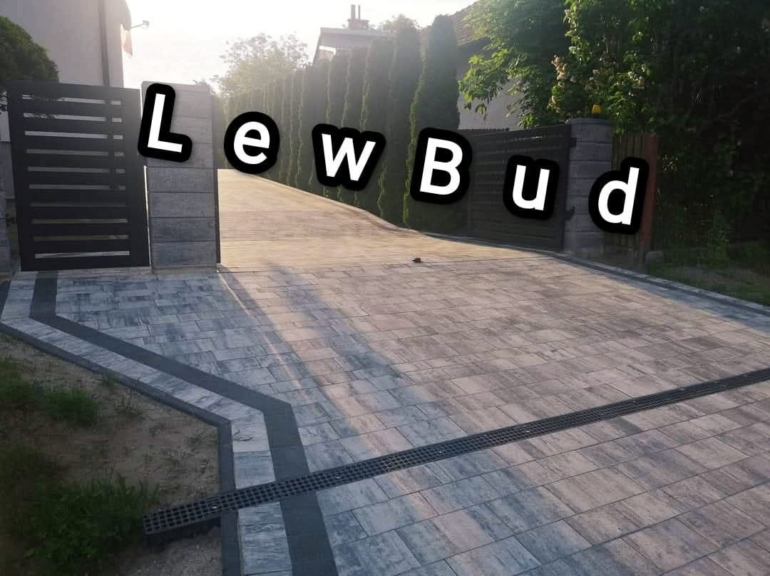 Ułożona kostka brukowa na podjeździe z odpływem liniowym, widok zza otwartej bramy wjazdowej.