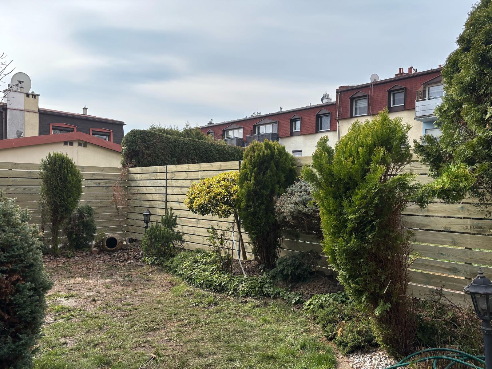 Nowo zamontowane, poziome ogrodzenie panelowe z impregnowanego drewna w ogrodzie z widocznymi tujami i elementami małej architektury ogrodowej.