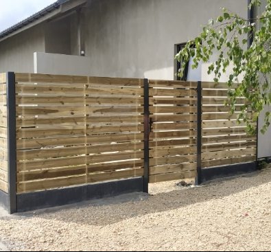 Drewniane ogrodzenie poziome z metalowymi słupkami, widok z zewnątrz na żwirową nawierzchnię i fragment domu w tle.