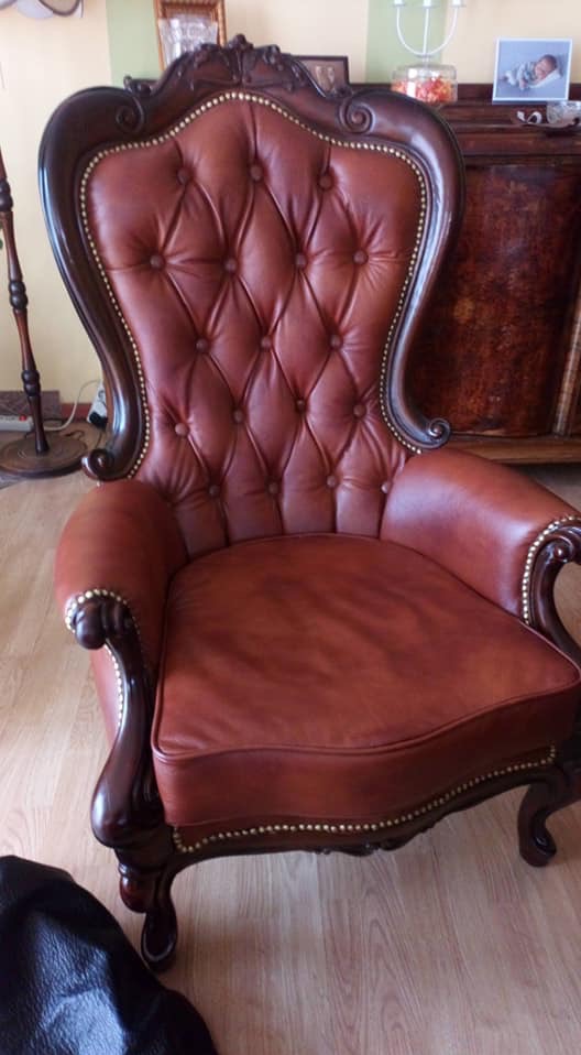 Odnowiony, skórzany fotel w stylu Ludwika Filipa, z pikowanym oparciem i ozdobnymi ćwiekami, stojący na drewnianej podłodze.