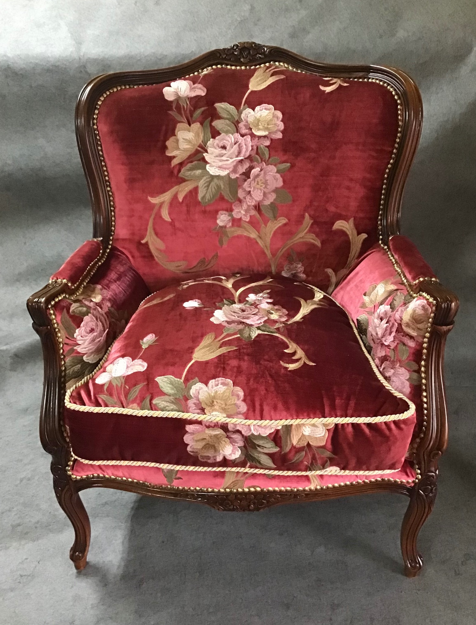 Elegancki fotel w stylu Ludwika XV z bordową, aksamitną tapicerką zdobioną motywem róż, wykończony drewnianą ramą z delikatnymi rzeźbieniami i ozdobnymi gwoździami.