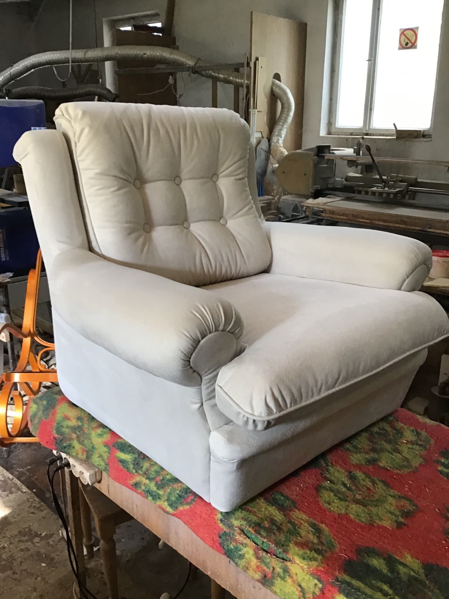 Kremowy fotel z guzikami na oparciu, stojący na stole z wzorzystym obrusem w warsztacie tapicerskim.