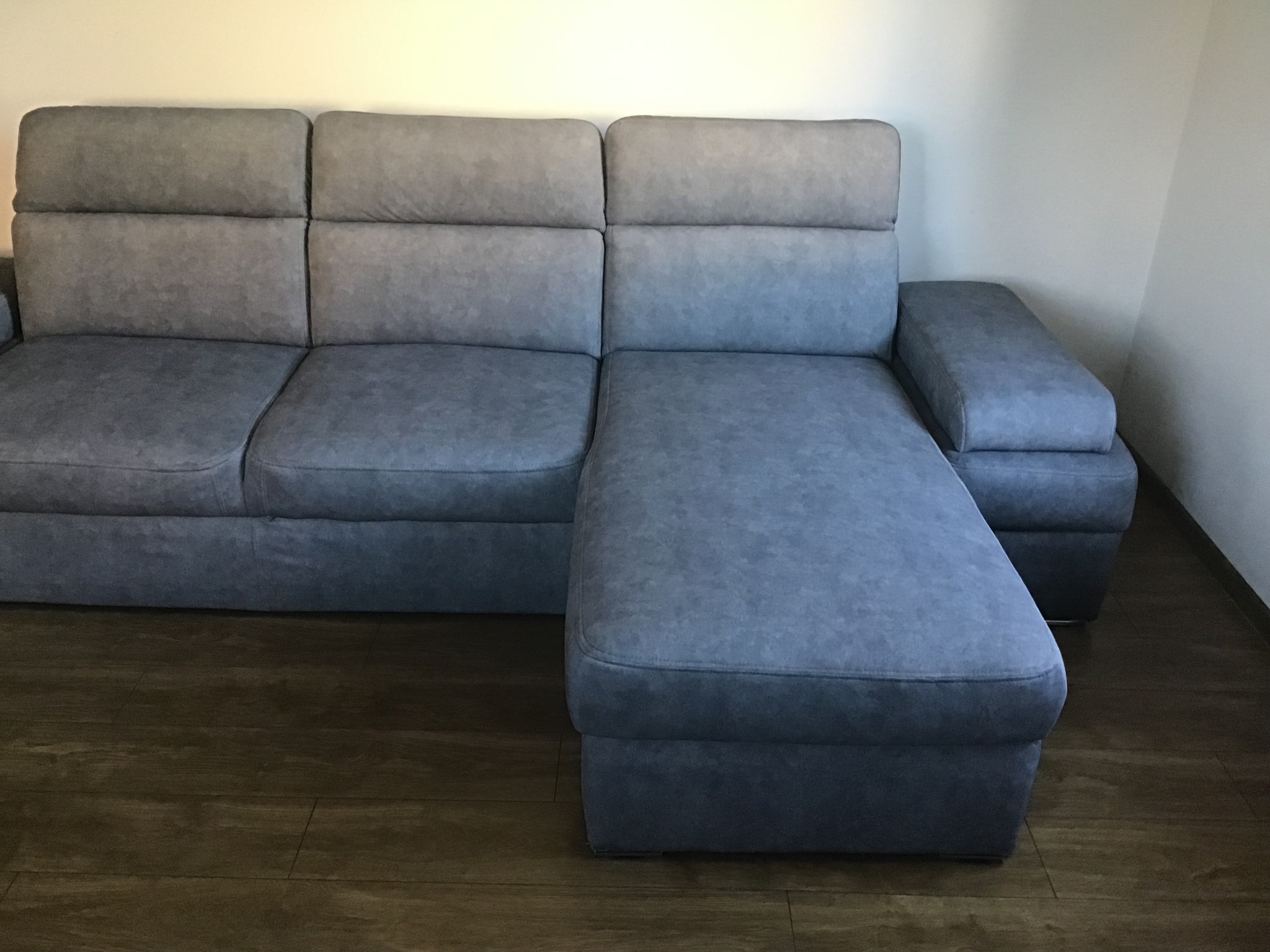 Szary narożnik z funkcją leżanki, modułową konstrukcją i wysokimi poduszkami oparciowymi, ustawiony na drewnianej podłodze.