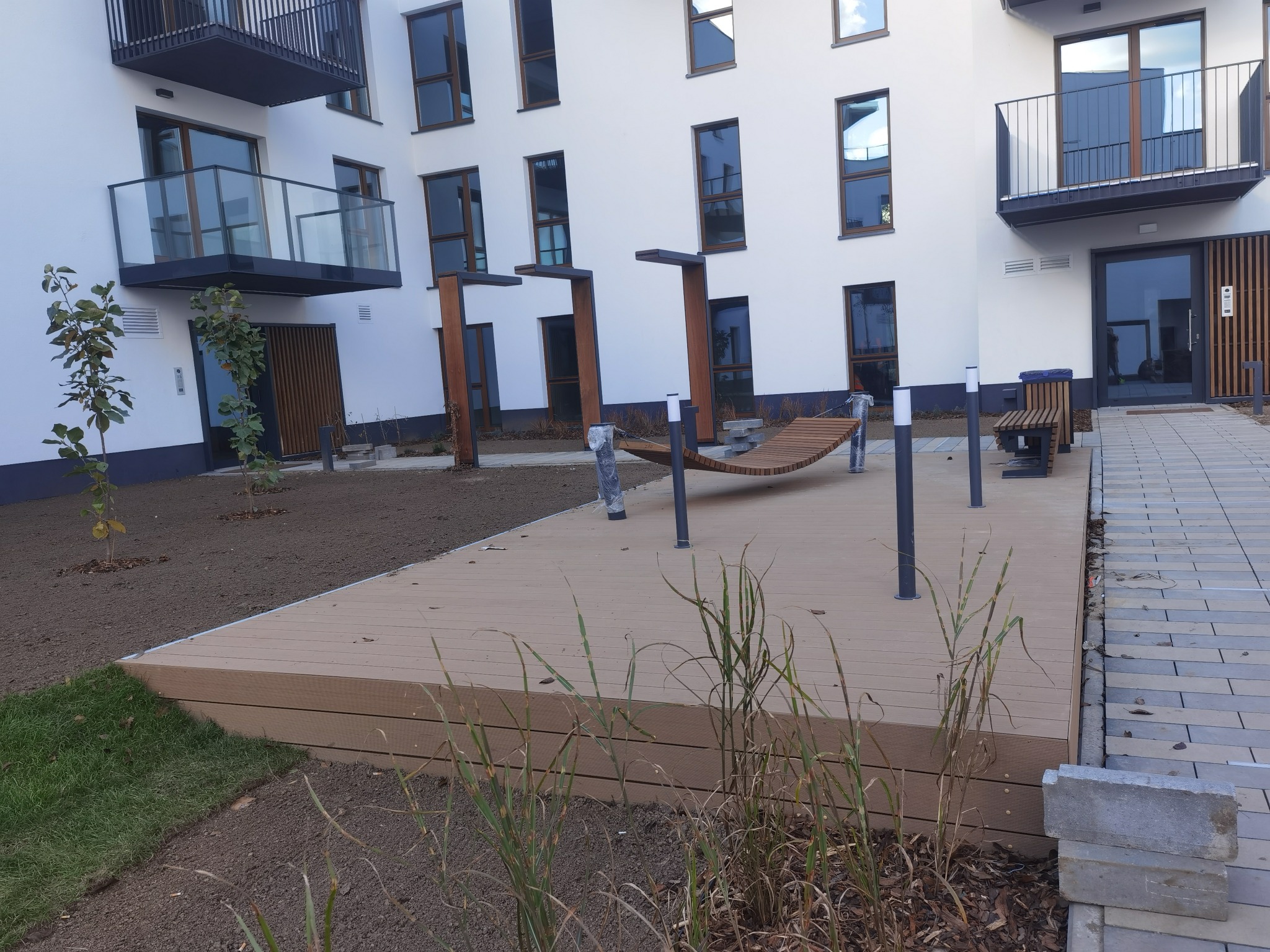 Nowoczesny taras kompozytowy z hamakiem na tle białego budynku wielorodzinnego z balkonami.