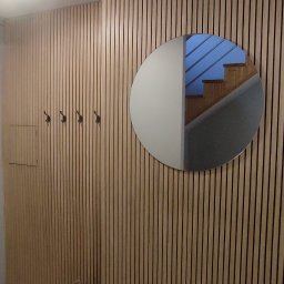 Jarosław Janik - Drewniana ściana z pionowych paneli z lustrem w kształcie koła, w którym odbijają się schody. Dekoracyjna latarenka i wieszaki na ubrania.