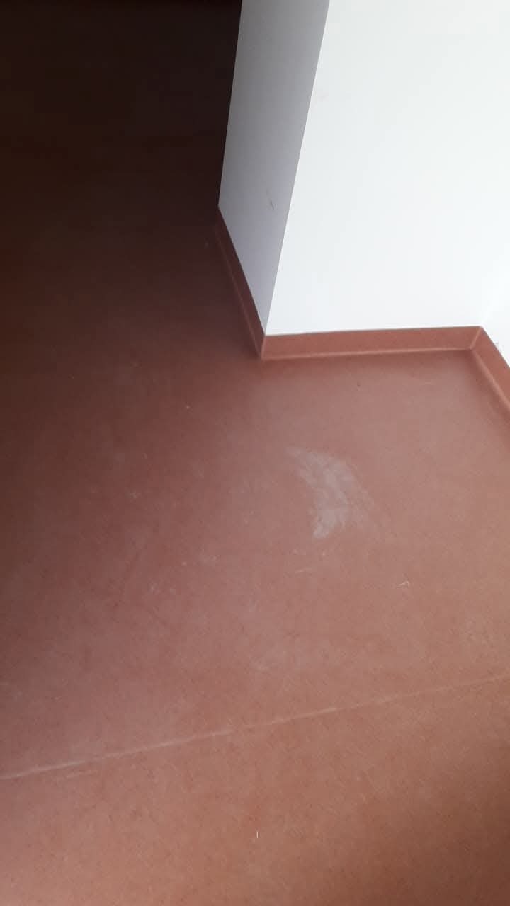 Czerwono-brązowa wykładzina PCV po montażu, widoczna przy białej ścianie z brązowymi listwami przypodłogowymi.