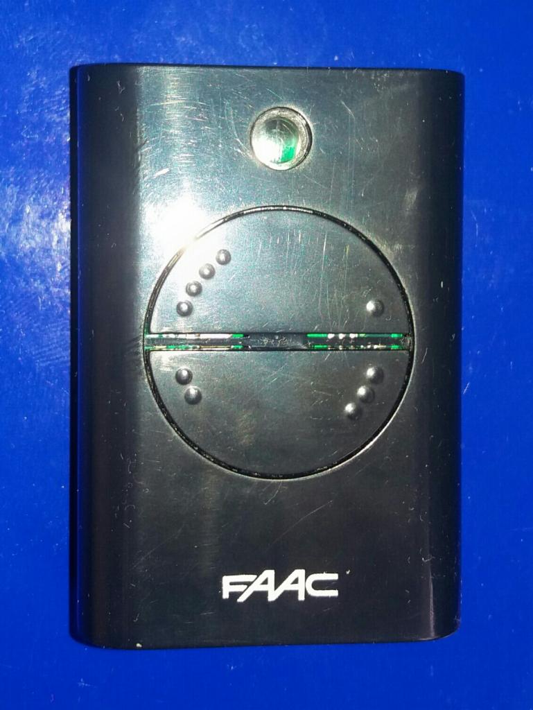 Czarny pilot do bramy marki FAAC z widocznymi śladami użytkowania, leżący na niebieskim tle.