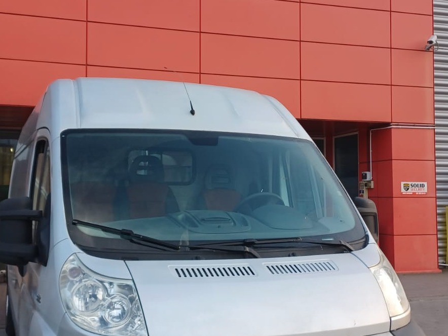 Srebrny van zaparkowany przed budynkiem o pomarańczowej fasadzie z widoczną kamerą monitoringu i logo firmy ochroniarskiej 'Solid Security'.