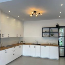 Geso Steel - Nowoczesna kuchnia z białymi szafkami, drewnianym blatem i czarnymi akcentami, takimi jak armatura i metalowa rama drzwi.