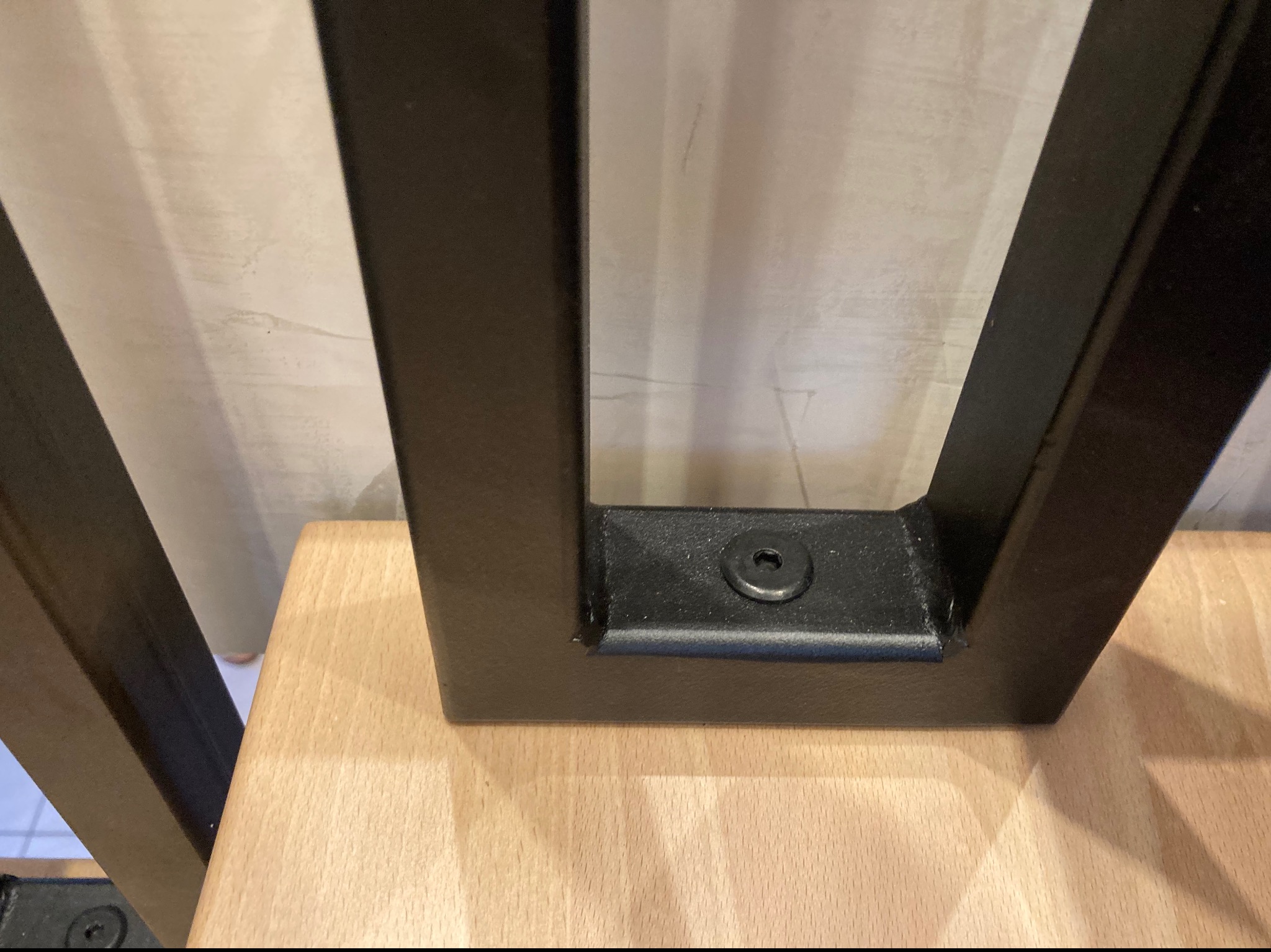 Detal metalowej nogi stołu z widocznym mocowaniem do drewnianego blatu, spawane łączenie, czarna farba proszkowa.