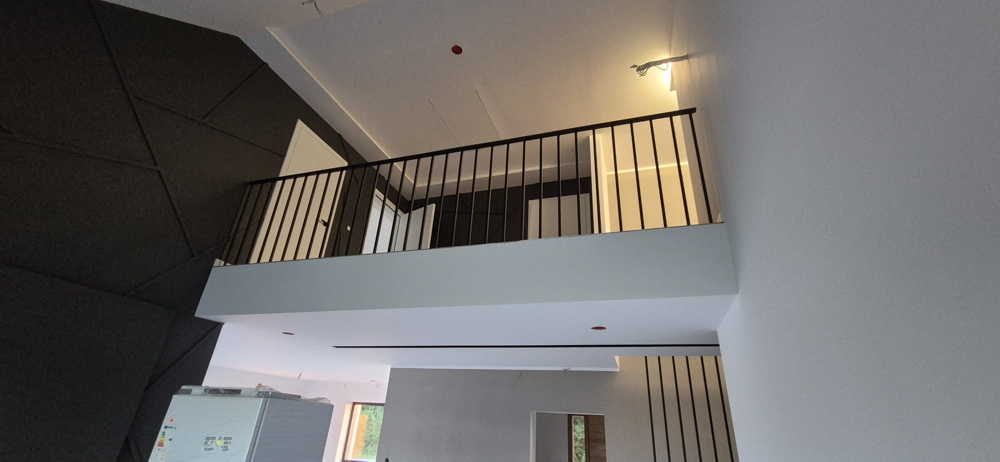 Nowoczesna, czarna balustrada z metalowymi prętami na antresoli w jasnym wnętrzu z elementami dekoracyjnymi na ścianie. Minimalistyczny design.