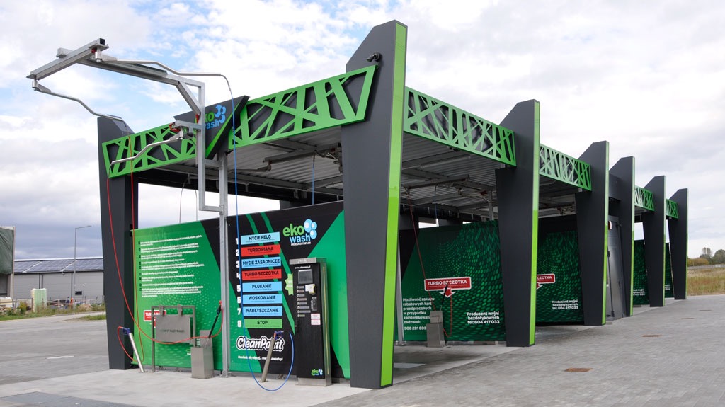 Nowoczesna, samoobsługowa myjnia samochodowa z konstrukcją w kolorach czerni i jaskrawej zieleni, widok na stanowiska mycia z urządzeniami i panelami sterowania.