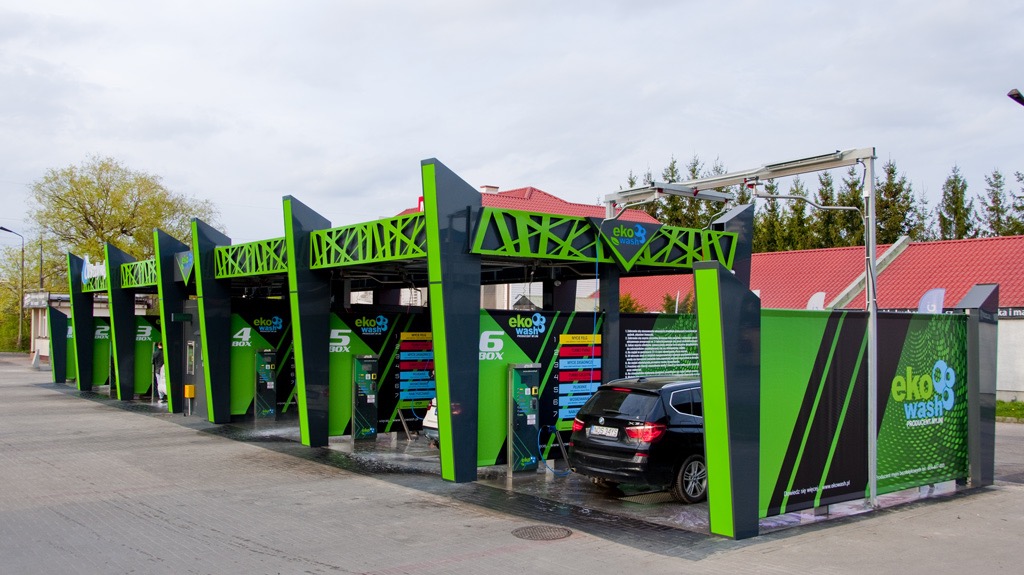 Samoobsługowa myjnia samochodowa z sześcioma stanowiskami w odcieniach szarości i zieleni, z czarnym SUV-em zaparkowanym przed stanowiskiem numer 6.