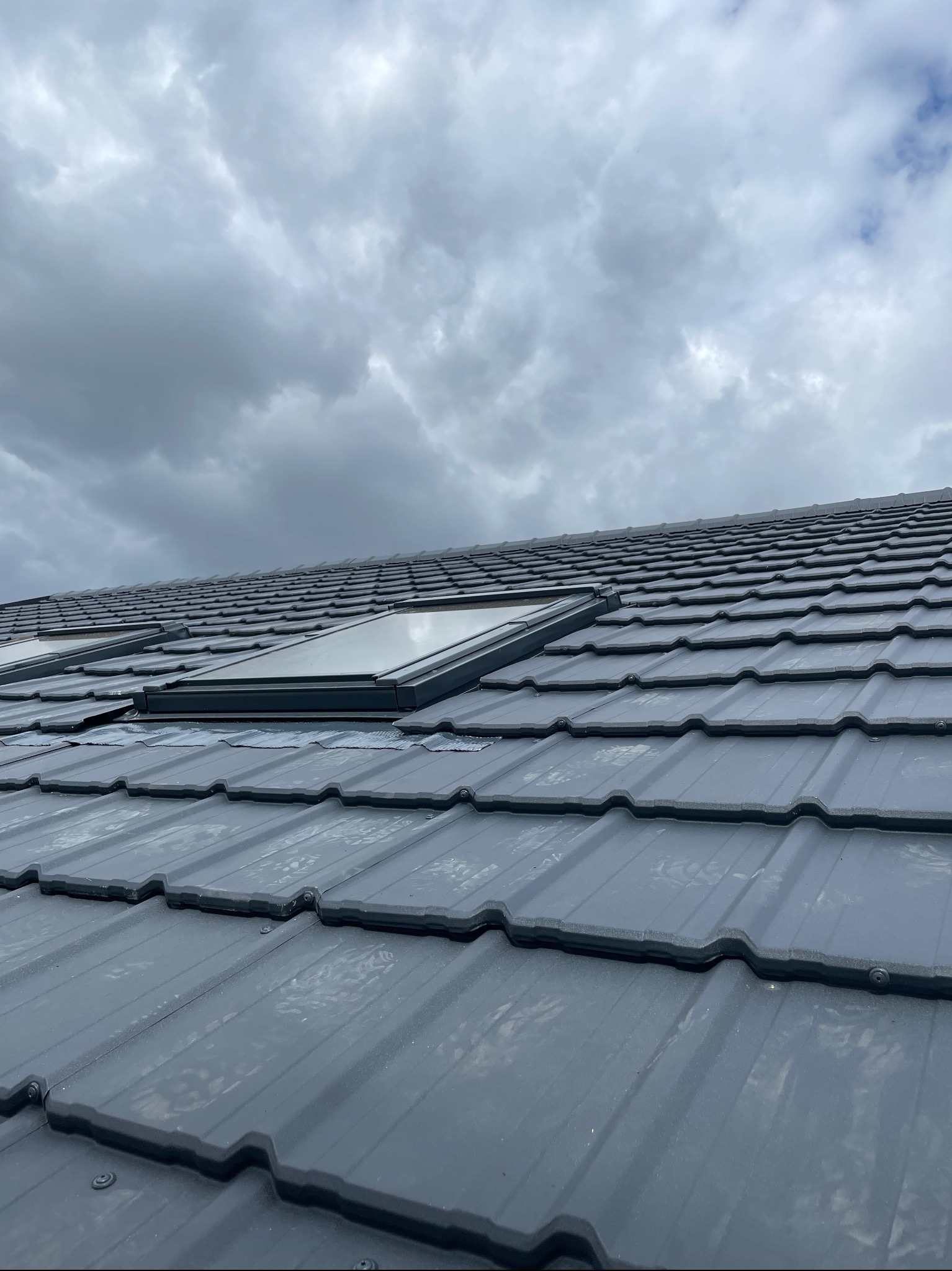 Szary dach z blachy z trzema oknami dachowymi, widok z dołu na tle pochmurnego nieba.