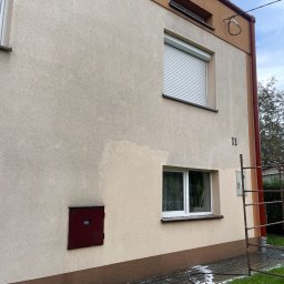 Jarosław Łukasiewicz - Fragment elewacji budynku z numerem 11, częściowo umyta, ukazująca różnicę w kolorze. Widoczne okna, roleta, skrzynka i fragment kostki brukowej z resztkami piany.