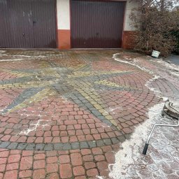 Jarosław Łukasiewicz - Mycie kostki brukowej z wzorem gwiazdy w Przemyślu. Częściowo umyta powierzchnia z użyciem myjki ciśnieniowej. Widoczne dwie bramy garażowe w tle.