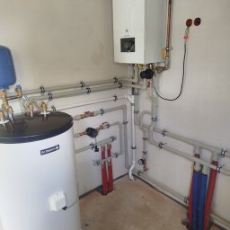 SANTERM - Nowoczesna kotłownia z białym kotłem gazowym De Dietrich i zasobnikiem ciepłej wody, z precyzyjnie ułożonymi rurami grzewczymi i hydraulicznymi na jasnej ścianie.
