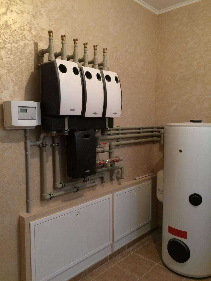 Kaskadowa instalacja grzewcza z trzema kotłami kondensacyjnymi, zasobnikiem ciepłej wody i sterownikiem, zamontowana na ścianie o fakturze dekoracyjnej.