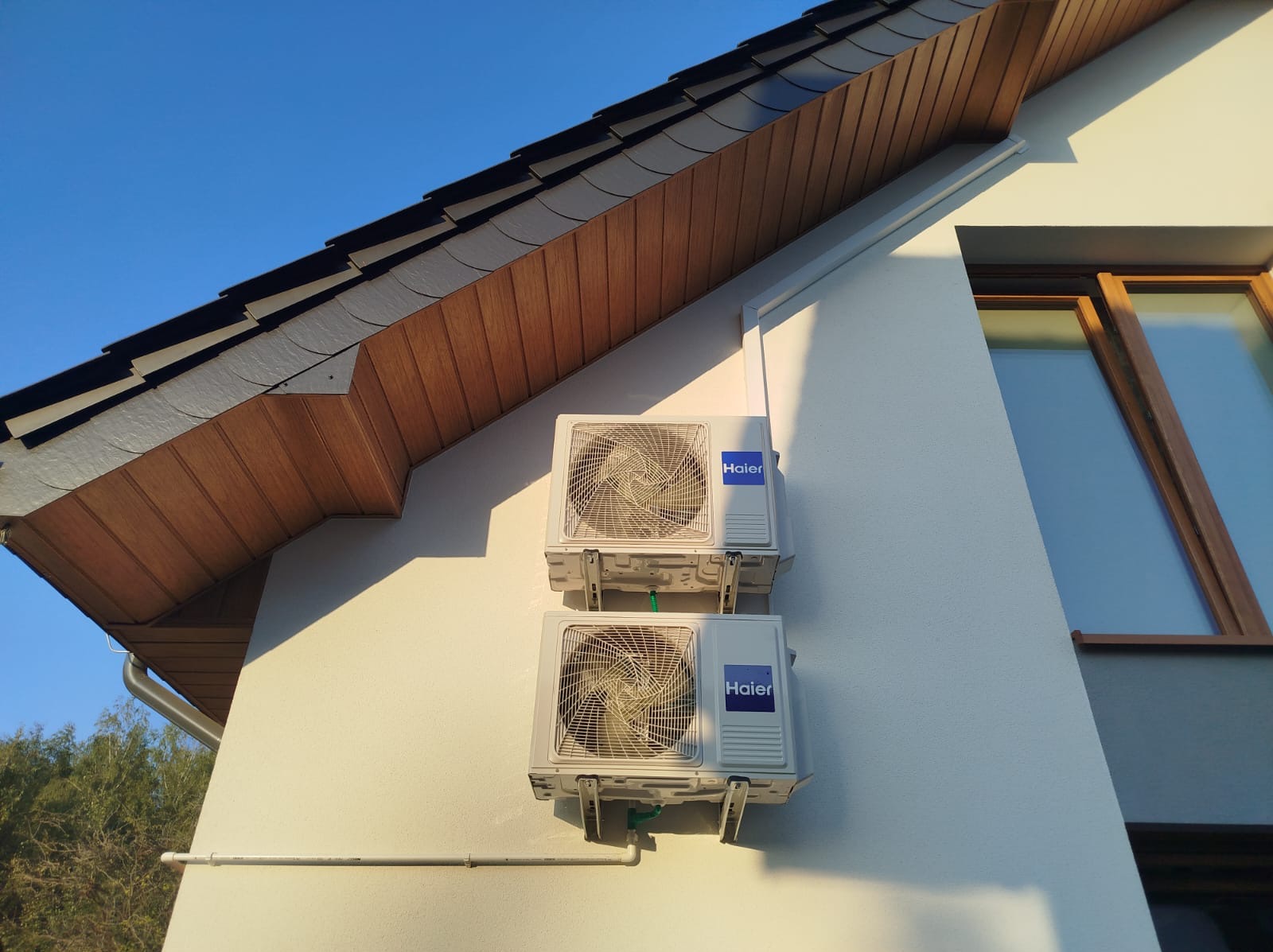 Dwa klimatyzatory Haier zamontowane jeden nad drugim na elewacji domu w Gdańsku, widoczne elementy dachu i okno.