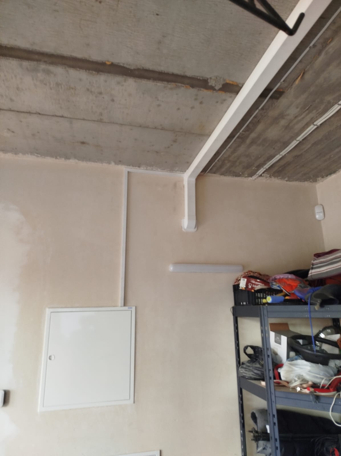 Białe rury wentylacyjne zamontowane pod betonowym sufitem w pomieszczeniu, widoczna szafka narzędziowa i skrzynka rewizyjna na ścianie.