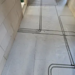 Elektryczne rury ochronne ułożone w bruzdach w podłodze z jasnych płytek podczas prac wykończeniowych w nowym budynku.