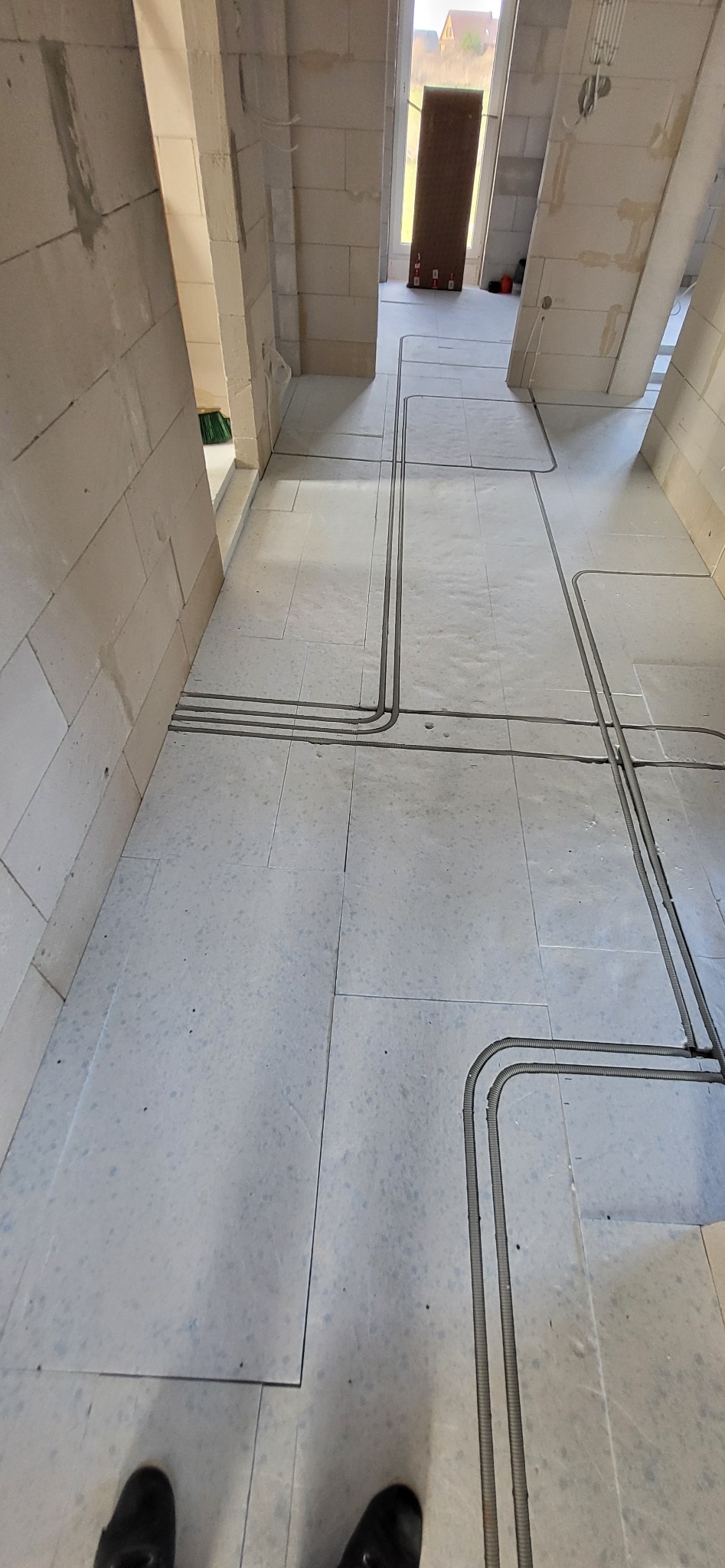 Elektryczne rury ochronne ułożone w bruzdach w podłodze z jasnych płytek podczas prac wykończeniowych w nowym budynku.